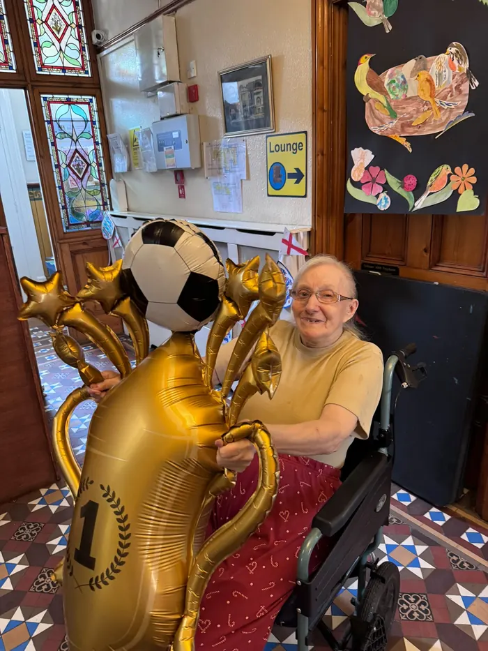 A resident smiling beside gold balloons and a football balloon