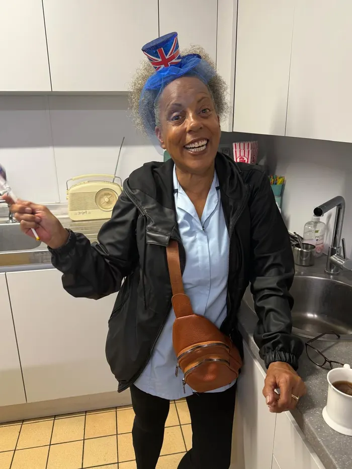 A member of the team in a Union Jack fascinator, smiling in the kitchen