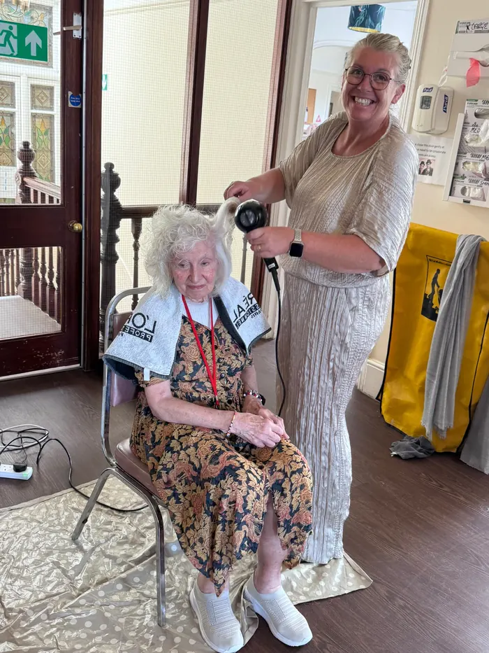 A resident having her hair blow-dried by a member of the team