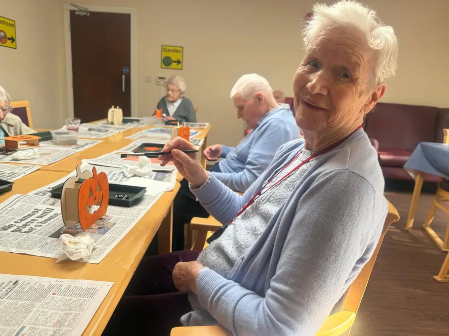 A resident smiling as she paints at a Halloween craft table
