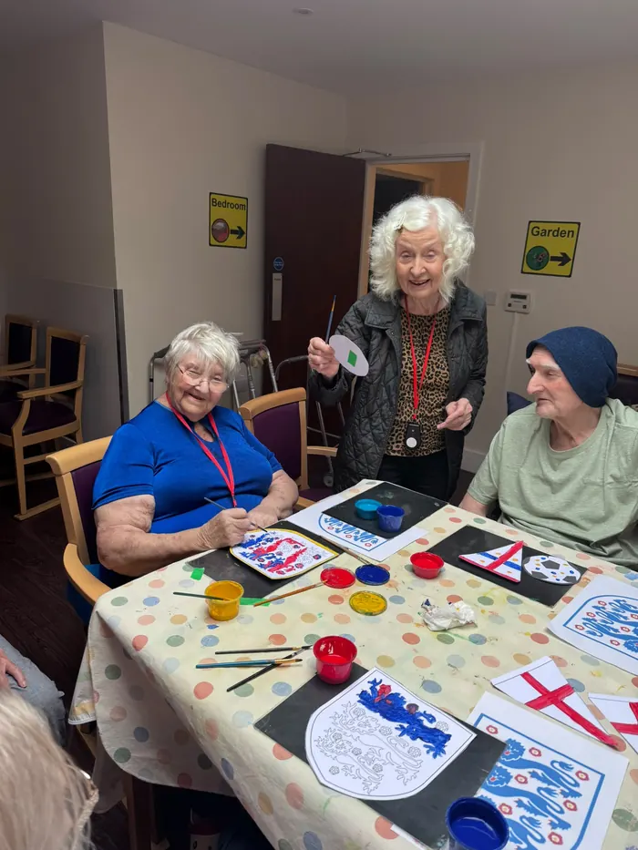 Three residents smiling around a table covered in paints and England flag artwork