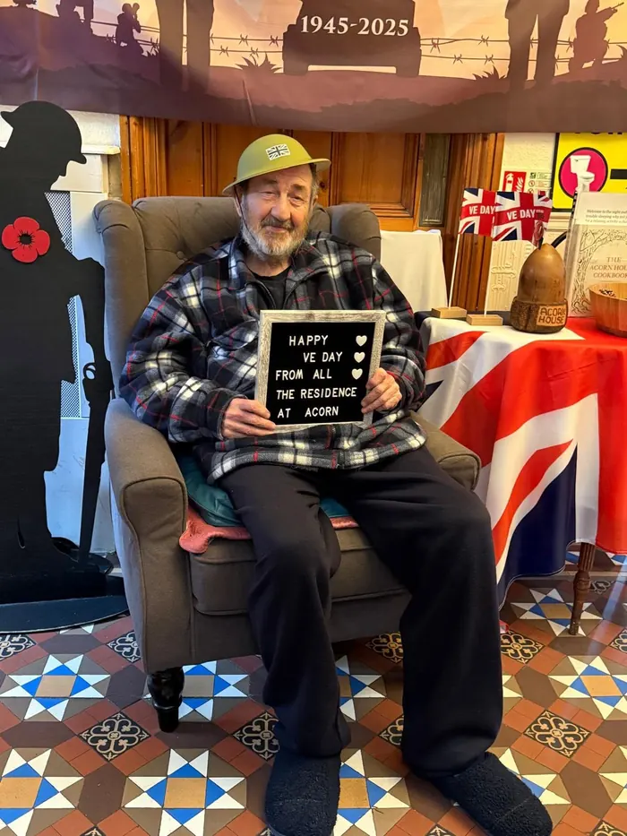 A resident holding a sign wishing everyone a happy VE Day from the residents at Acorn