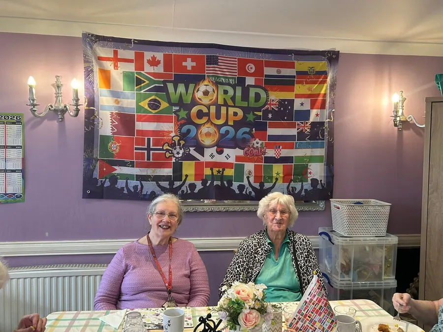 Two residents smiling at a table in front of a World Cup 2026 banner